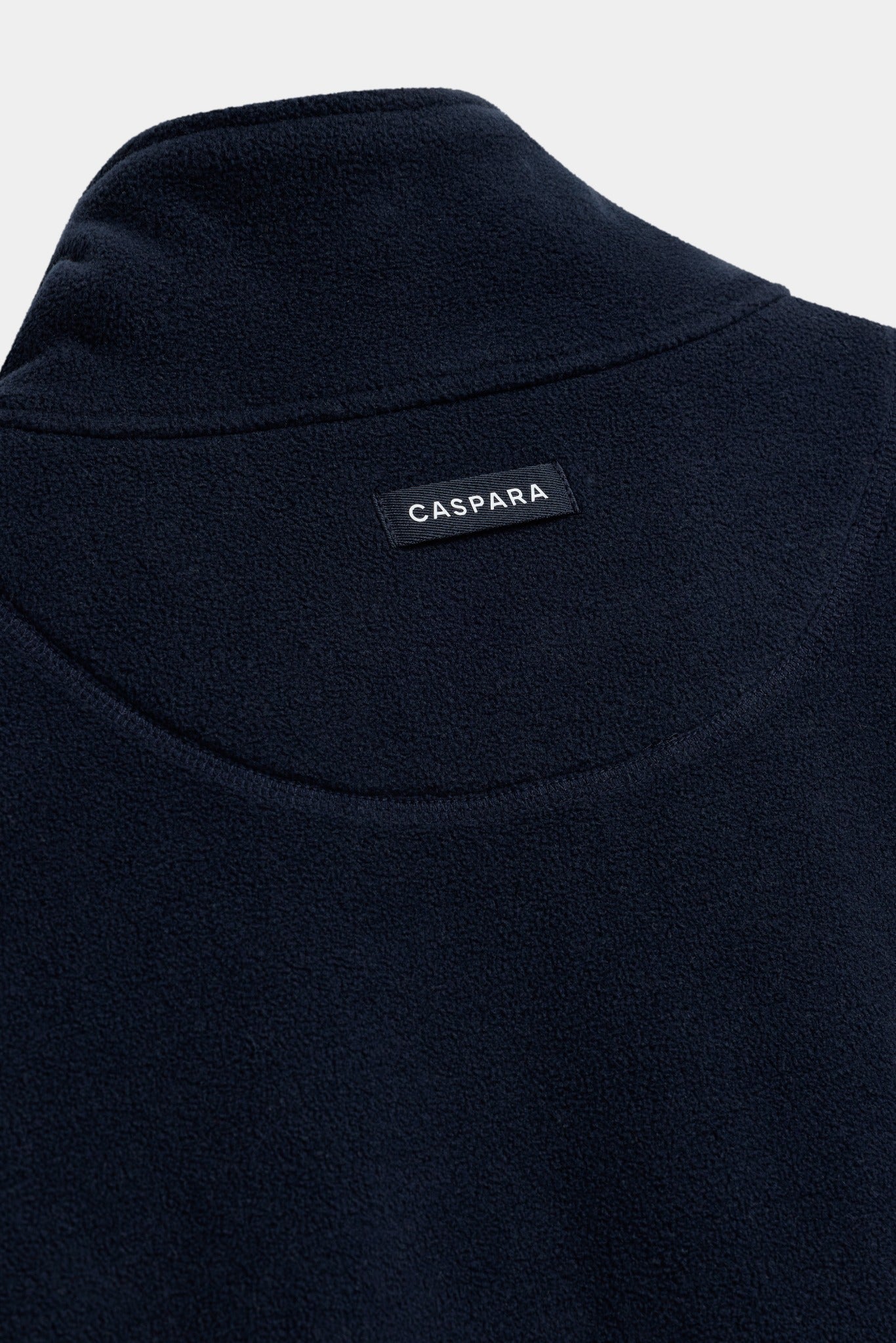 Close-up of the CASPARA logo tab on the back collar of a navy polar fleece pullover.